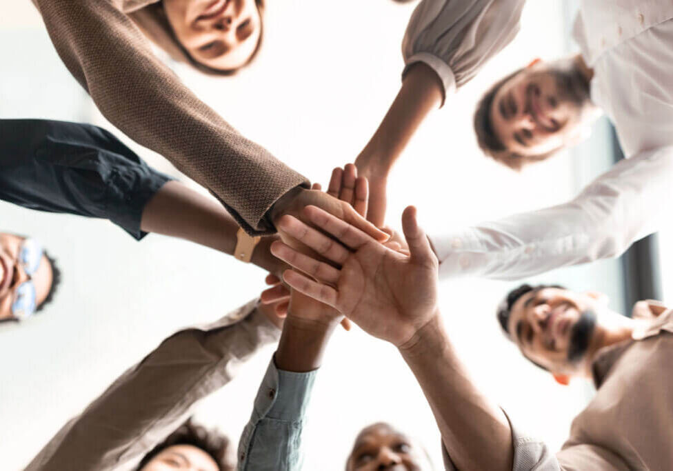Teambuilding, Teamwork And Unity Concept. Below view of diverse group of smiling people putting their hands together, standing in circle. Multiethnic colleagues celebrating collaboration and alliance